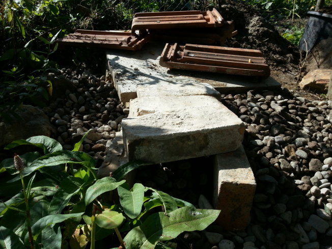 Damit ich die Zugangsritze für die Eidechsen nicht völlig zuschütte, wenn ich die Erde auffülle, habe ich diesen Tunnel aus Backsteinen gebaut. Rundherum habe ich 30 Zentimeter hoch groben Kies aufgebracht, damit das Wasser abfließen kann und zugleich ein Wurzelunkraut (bei mir wächst Giersch!!!) keine Chance hat, mein Bauwerk zu besiedeln.