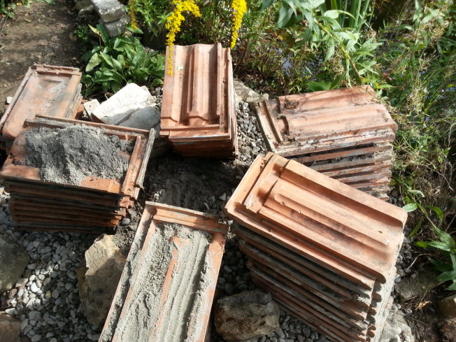 Alte Dachziegel dienen als Gerüst für die Eidechsenburg, und zugleich auch als Unterschlupf für Eidechsen, aber auch für Insekten. Ich habe sie extra so ausgerichtet, dass das Gefälle weg von der Mitte geht, damit das Regenwasser nicht unter die Ziegel fließt und sich dort sammelt. In der Mitte habe ich nach und nach mit Sand, Kies und erde aufgefüllt. Für Stabilität sorgten erste Bruchsteine, die ich im Feld gesammelt hatte.
